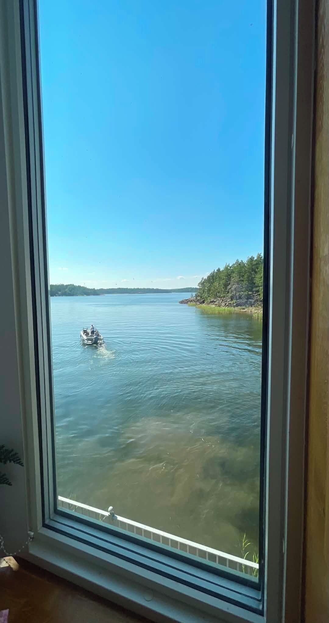 Vista a través de una ventana de un lago con un barco y una orilla arbolada.