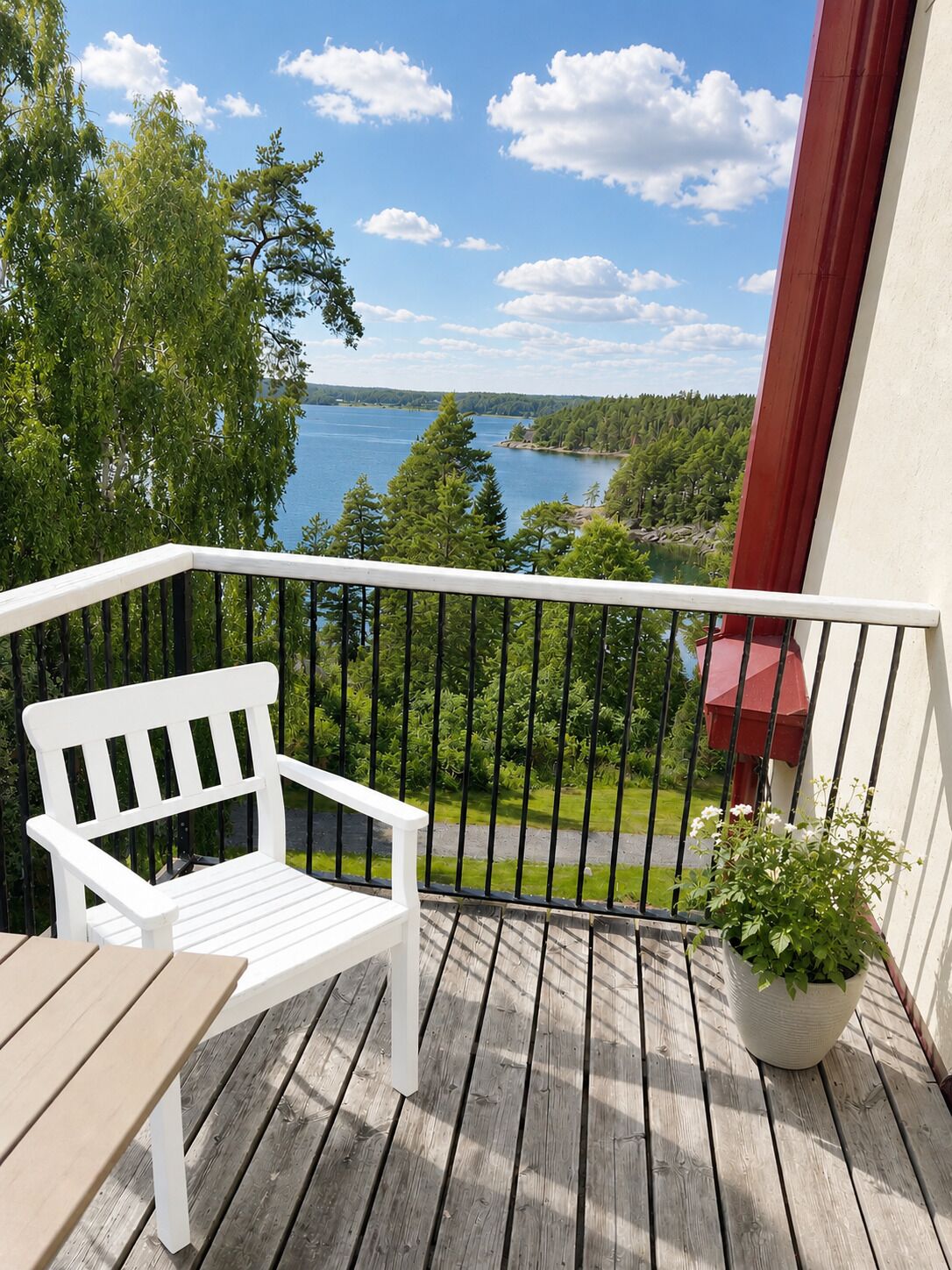 A wooden deck with a white bench and a potted plant, overlooking a lake and forested area.