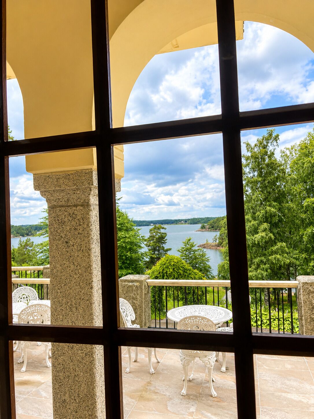A balcony with a view of a lake and trees, featuring a stone column and white outdoor furniture.