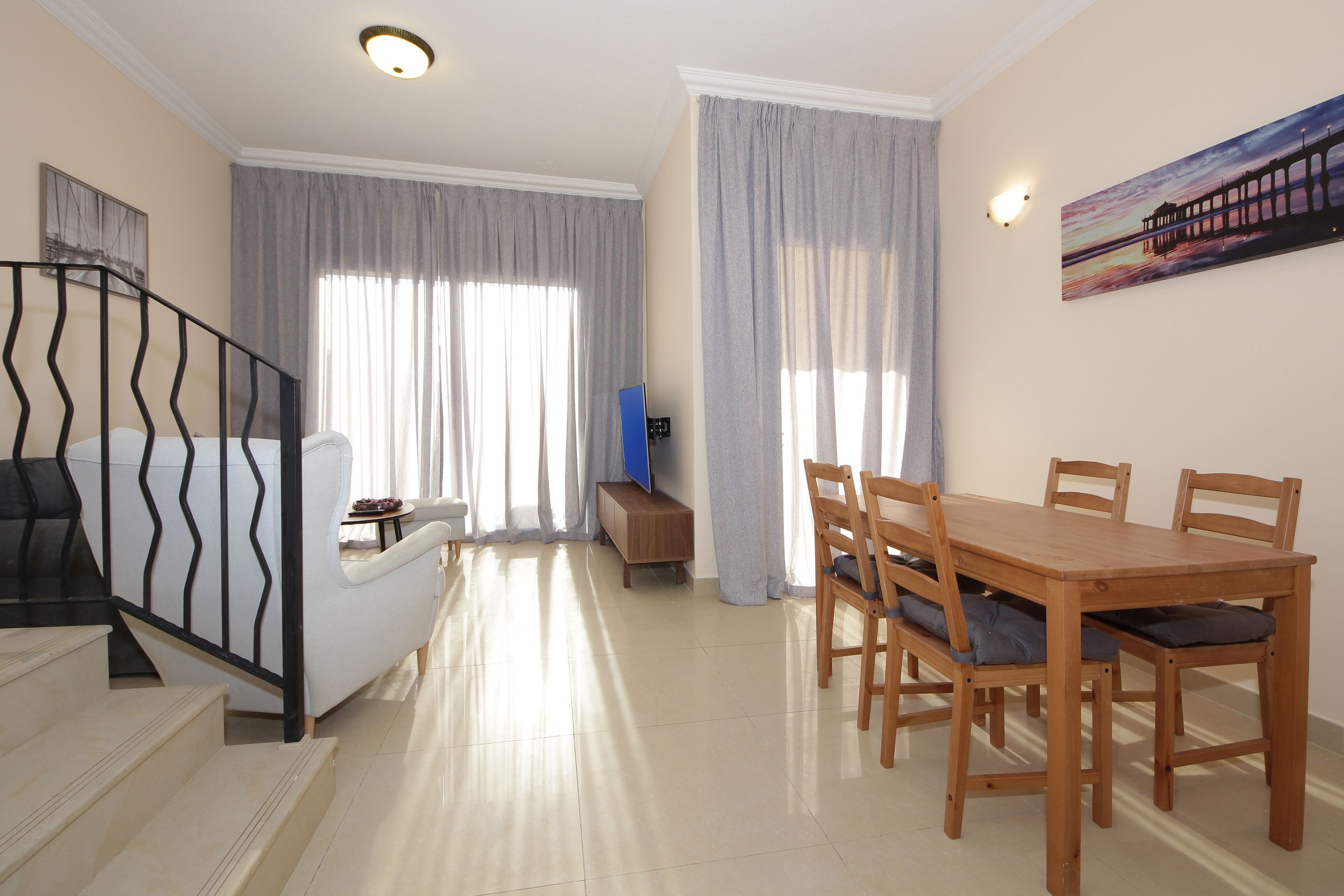 A spacious living area with a dining table, chairs, a sofa, and a staircase.