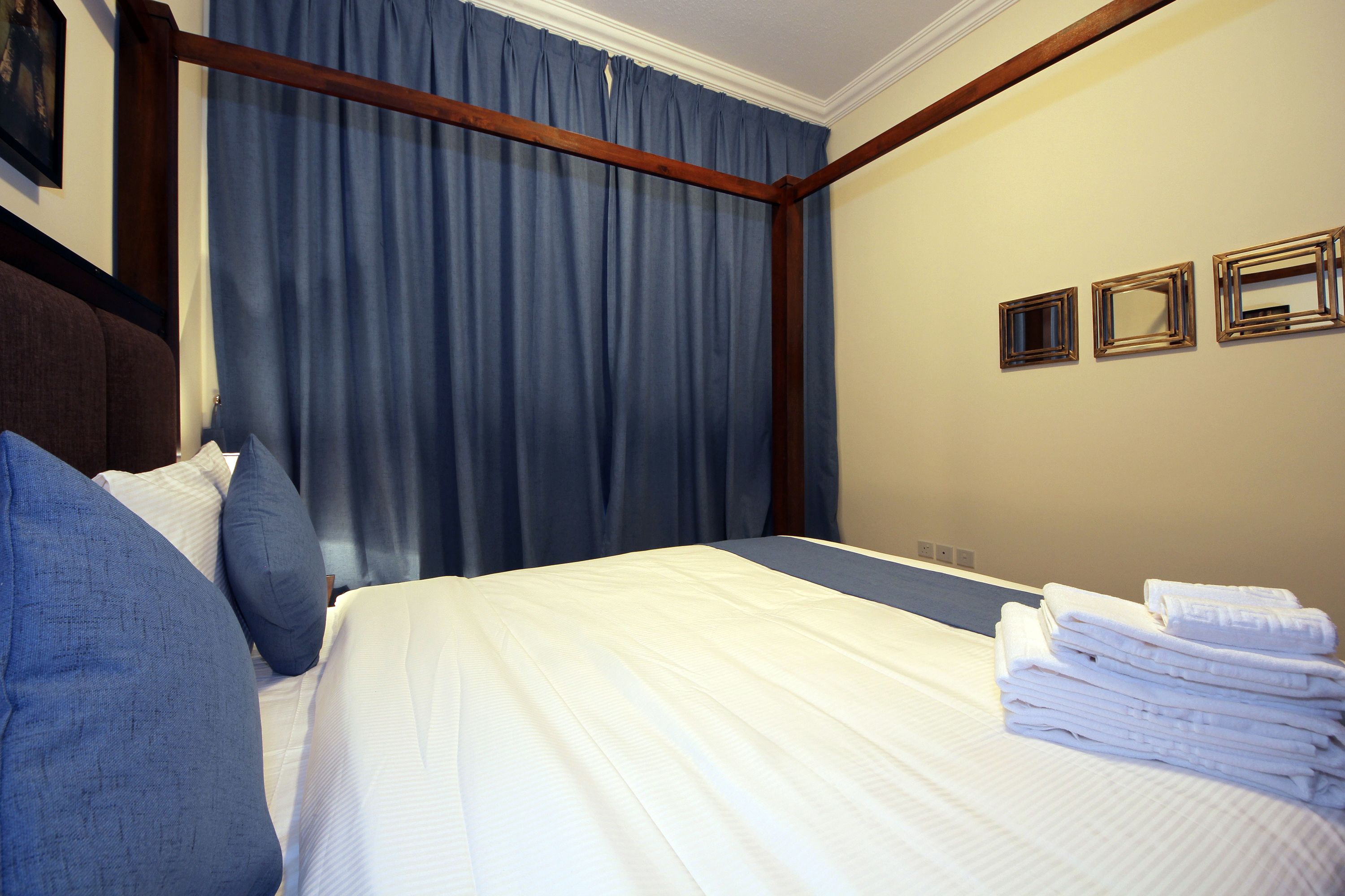 A hotel room with a bed, blue curtains, and a stack of towels.