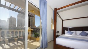 A bedroom with a four-poster bed, a balcony with a table and chairs, and a city view. - Piks Key- Al Hamra Village (Ras Al Khaimah)