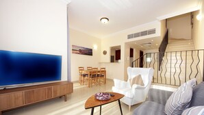 A modern living room with a flat-screen TV, a wooden cabinet, a grey sofa, a white armchair, and a dining area with wooden chairs and a table. - Piks Key- Al Hamra Village (Ras Al Khaimah)
