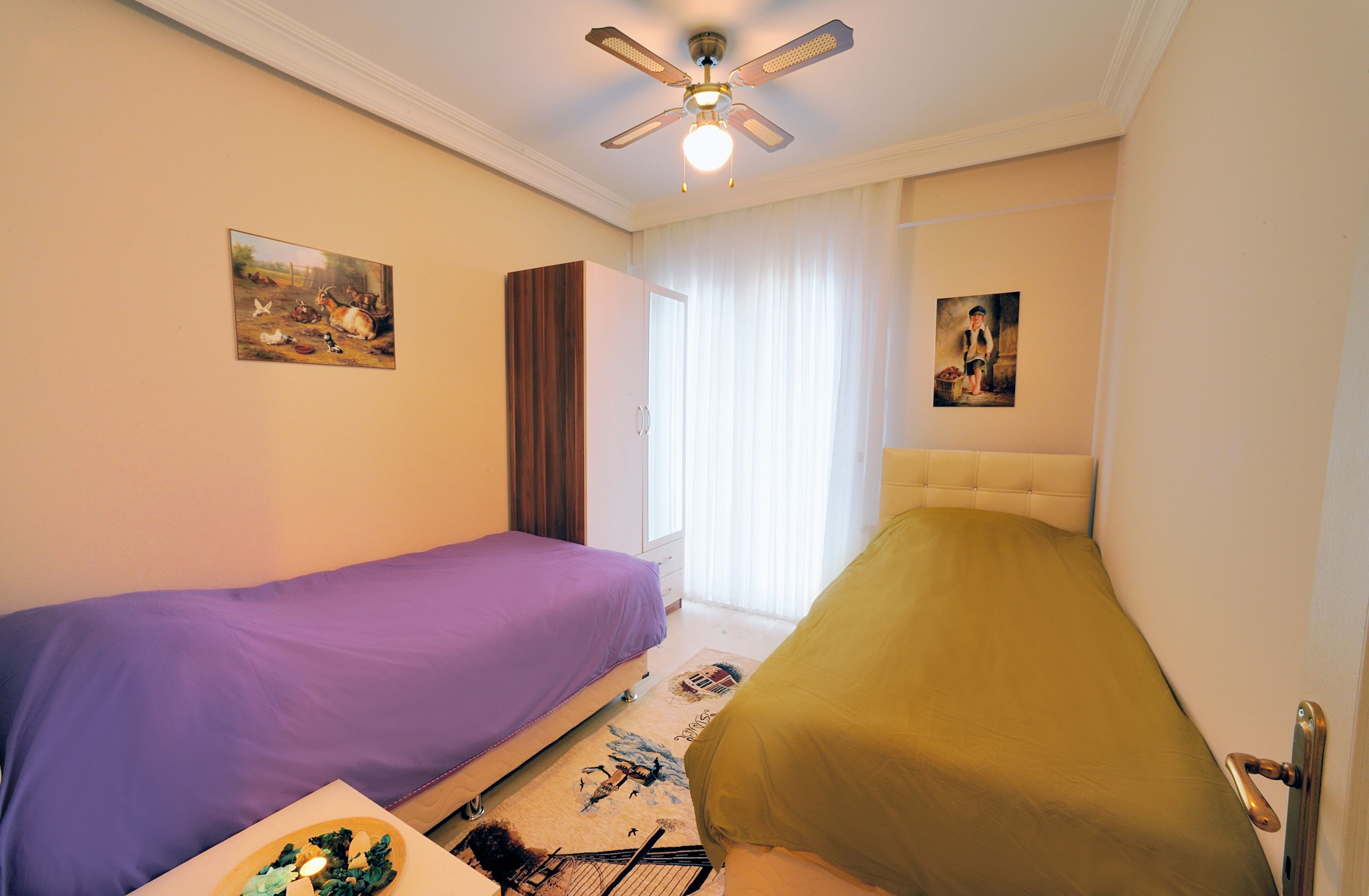 Una camera da letto con due letti, un ventilatore a soffitto e opere d'arte alle pareti.