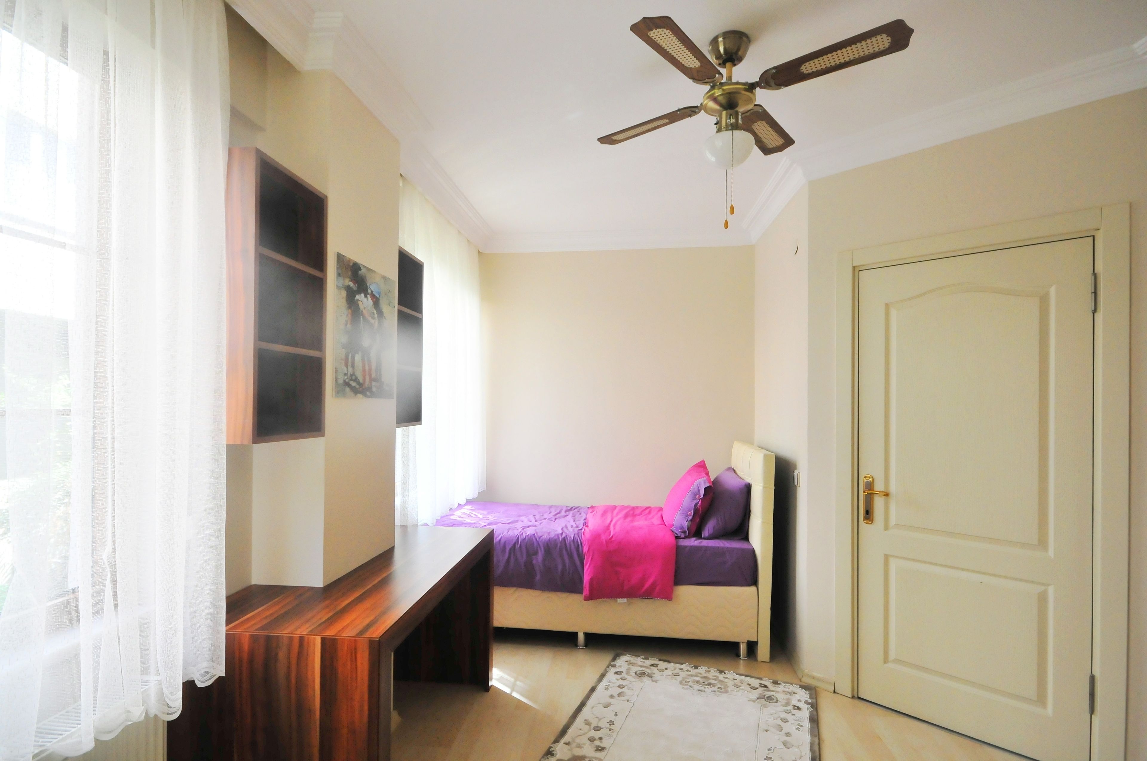 A bedroom with a bed, a ceiling fan, a door, and a window with curtains.