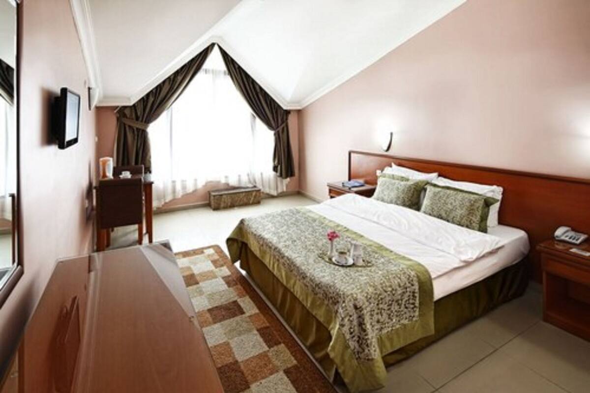 A hotel room with a large bed, a wooden desk, a small table with a tray, and a window with curtains.