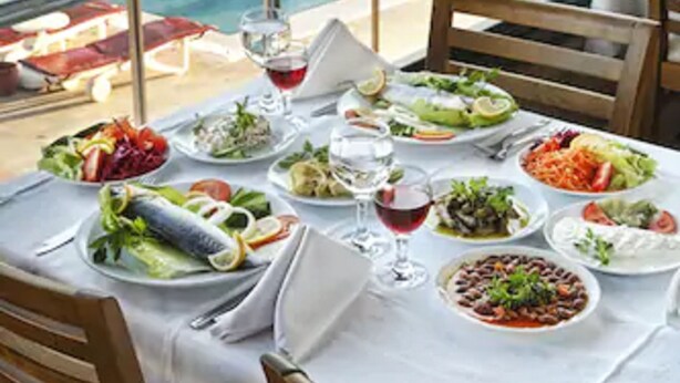 A dining table with various dishes and a glass of red wine, overlooking a pool with lounge chairs and umbrellas. - Halic Park Hotel (Ayvalik)