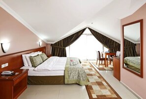 A bedroom with a bed, bedside table, chair, desk, and a large mirror. - Halic Park Hotel (Ayvalik)