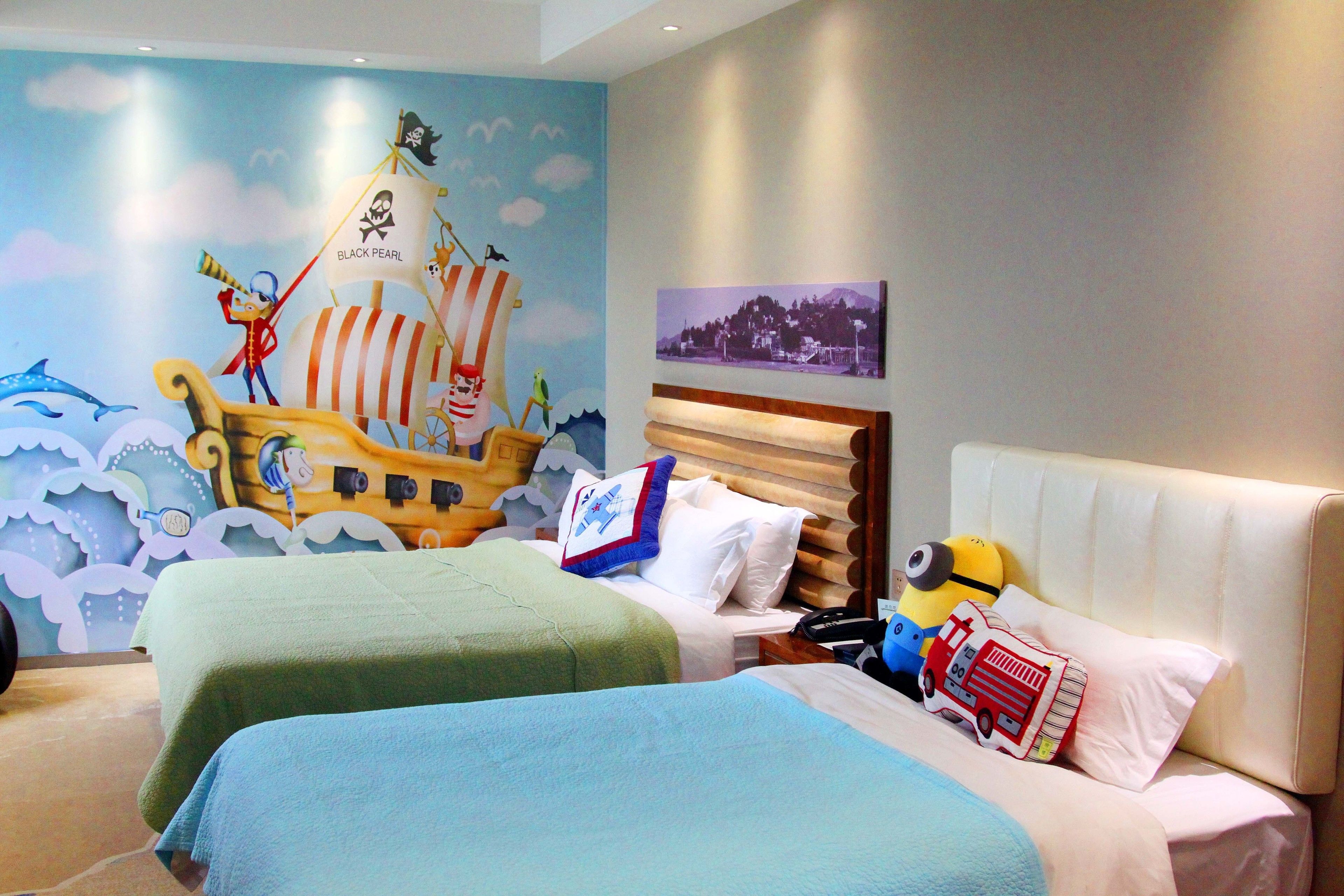 Une chambre d’hôtel avec deux lits, une fresque représentant un navire de pirates et un tableau représentant un paysage urbain accroché au mur.