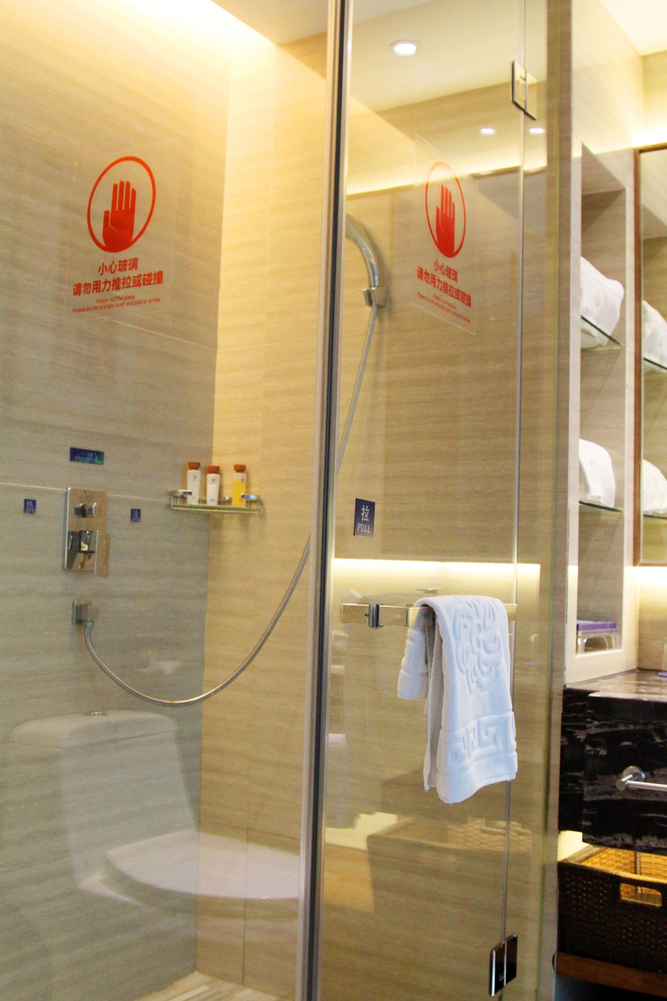 A modern bathroom with a glass shower enclosure, a towel rack, and a shelf with toiletries.