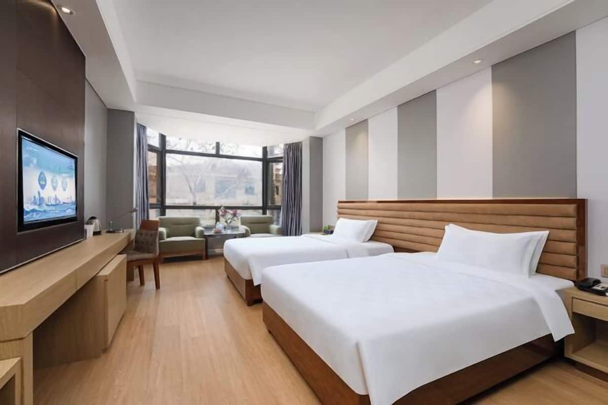 A hotel room with two beds, a TV, a sofa, a desk, and a window with a view.