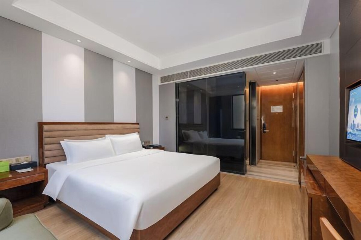 Une chambre d’hôtel moderne dotée d’un grand lit, d’une télévision, d’une table de chevet en bois et d’une porte coulissante donnant accès à la salle de bain.