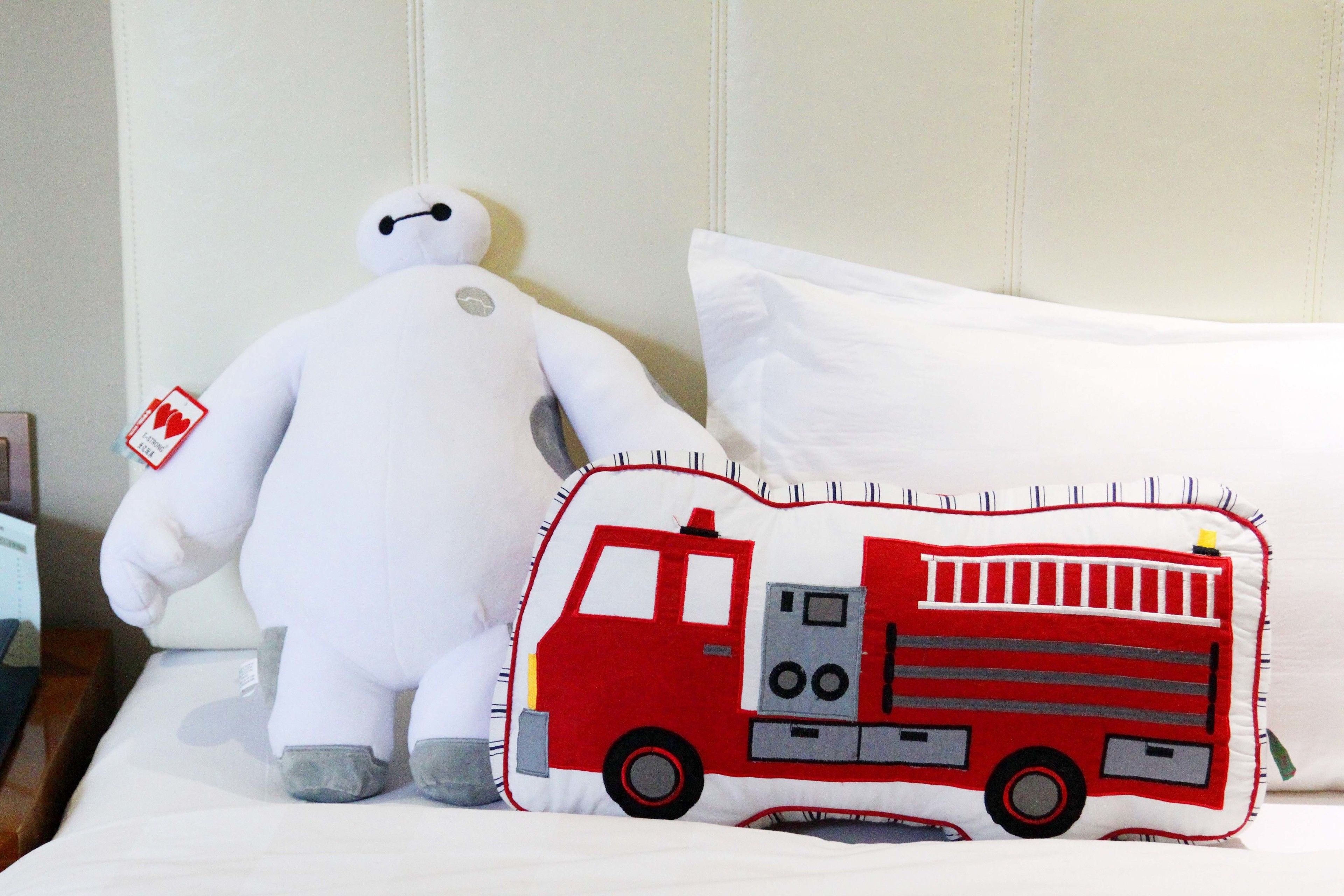 A bed with a white pillow and a pillow with a red fire truck design.