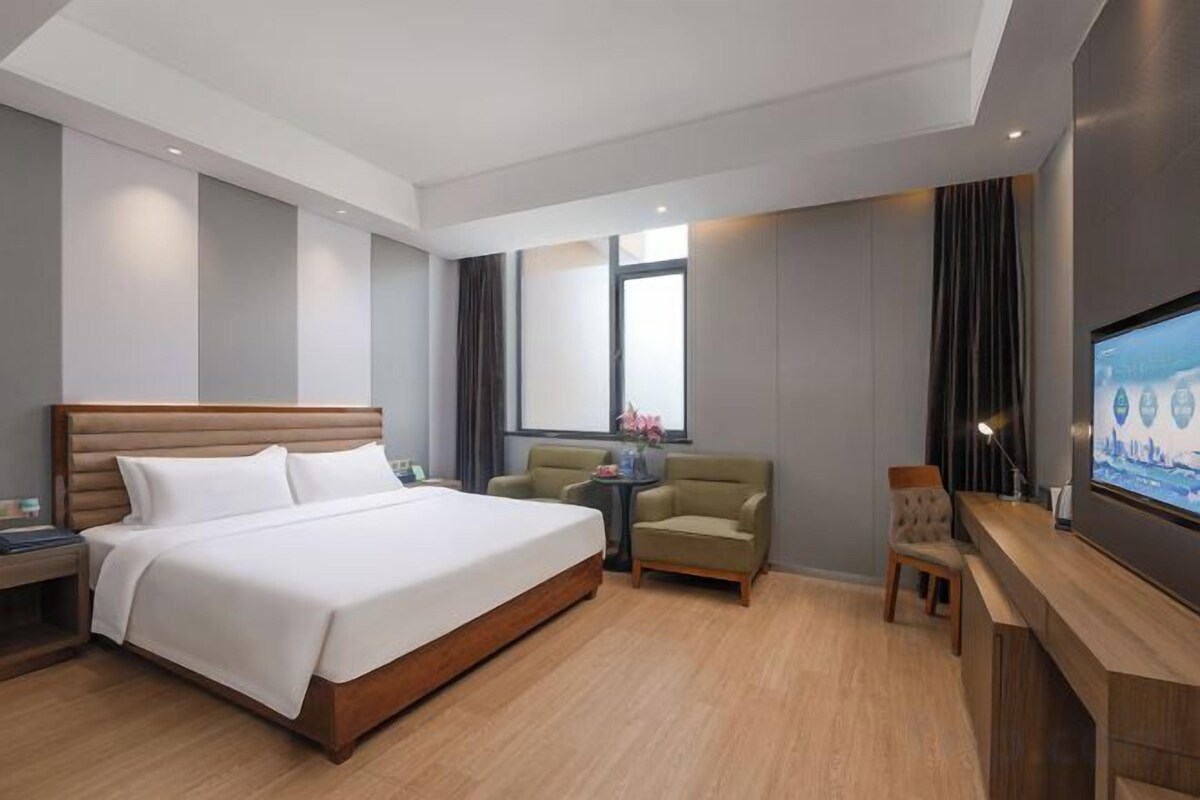 A hotel room with a large bed, a desk with a chair, a television, and a window with curtains.