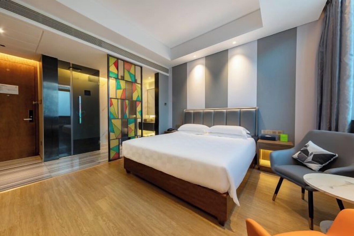 A modern hotel room with a large bed, a desk, and a sofa.