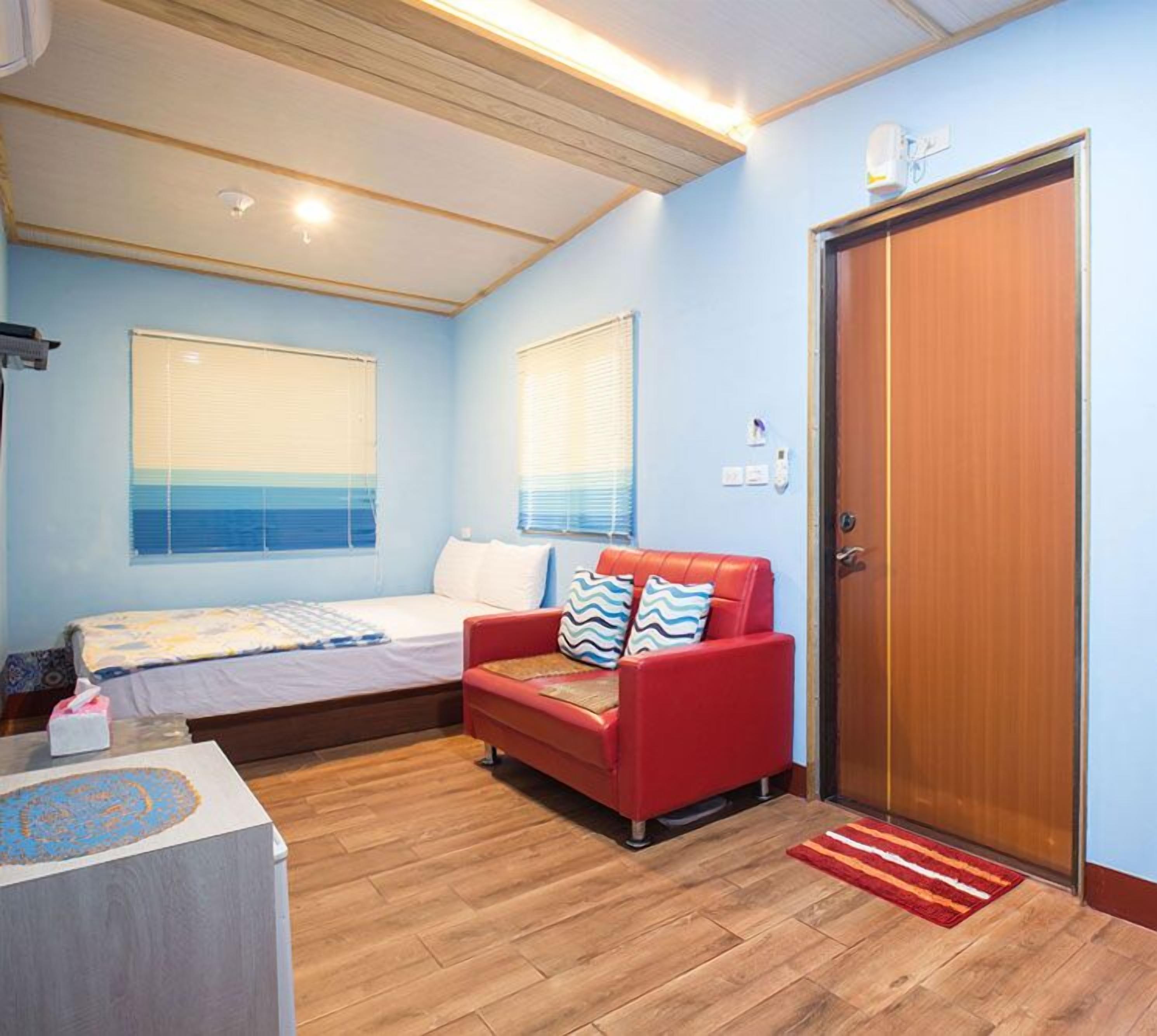 A room with a bed, a red sofa, a wooden floor, and a door.