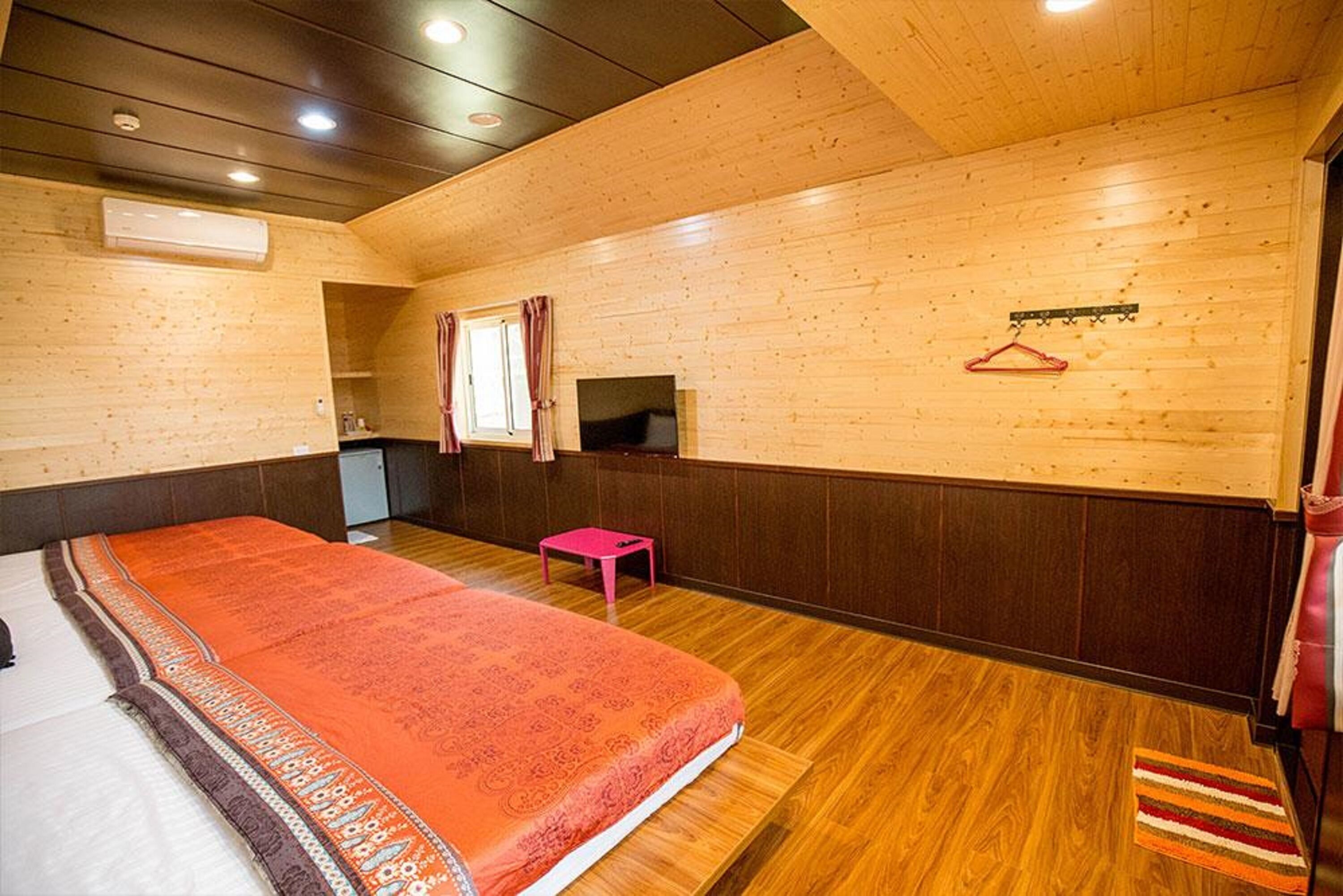 A wooden-paneled room with a bed, a small table, a TV, and a coat rack.