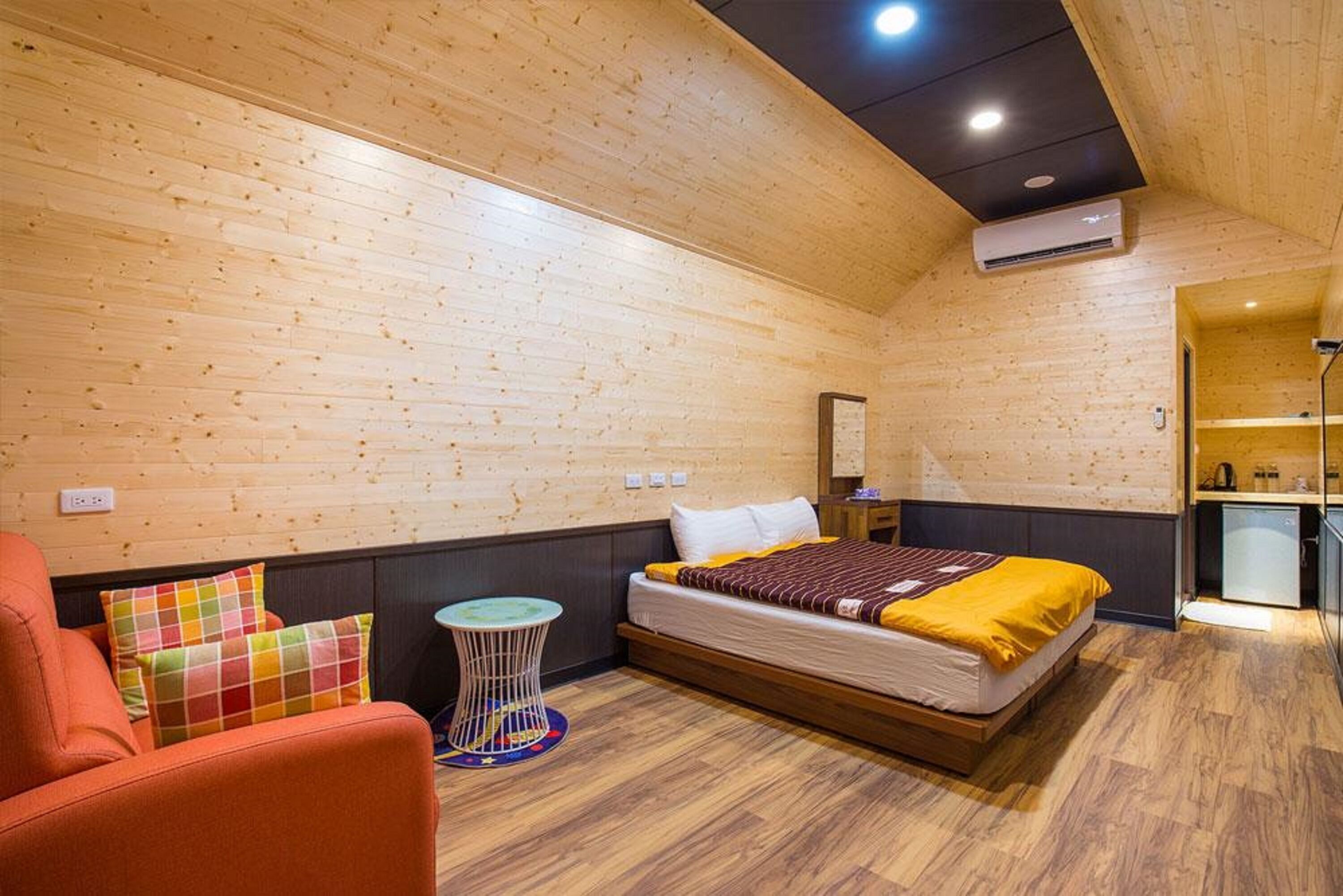 Une pièce avec un plafond en bois, un lit recouvert d’une couverture jaune, une petite table ronde et une chaise rouge.