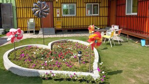 A house with a yellow exterior, a garden with a flower bed, and a windmill. - Happy House (Liuqiu)