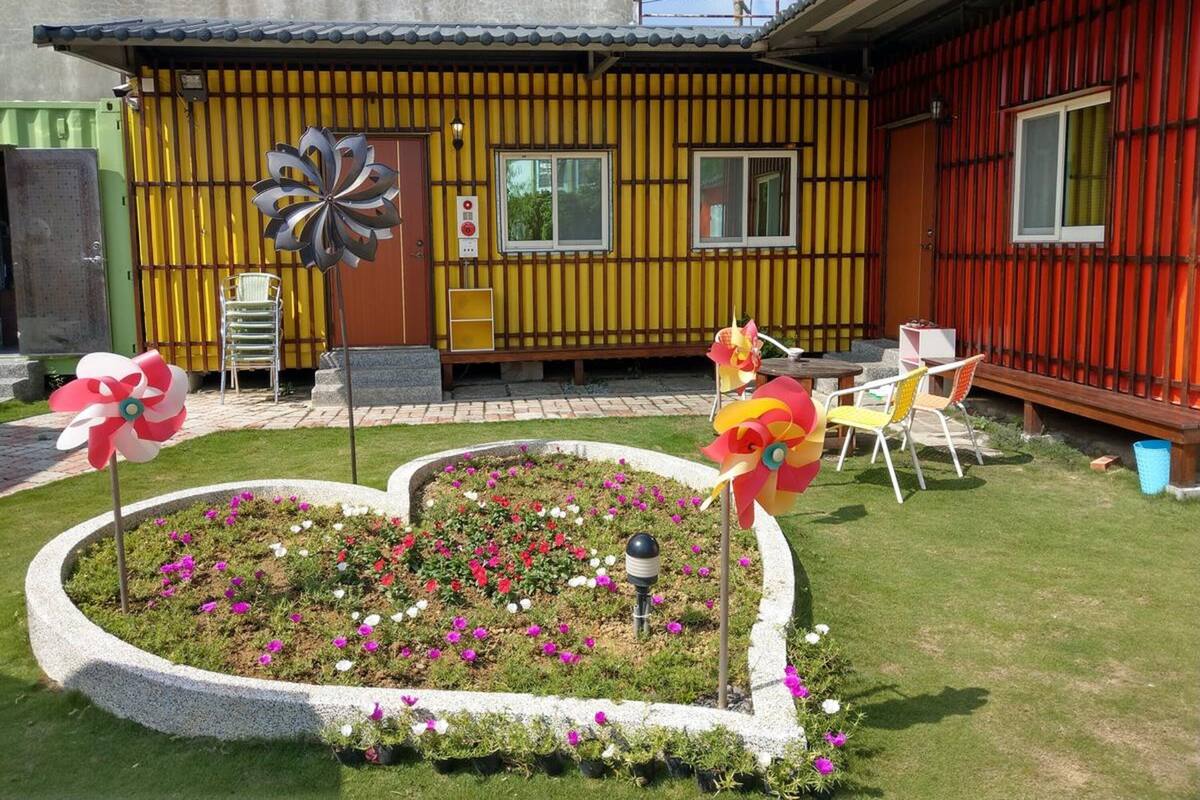 Una casa con fachada amarilla, un jardín con un parterre de flores y un molino.