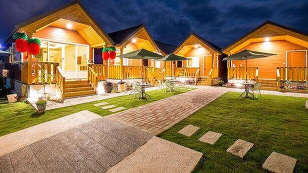 A row of wooden cabins with outdoor seating areas, each with a covered patio and a visible entrance. - Happy House (Liuqiu)
