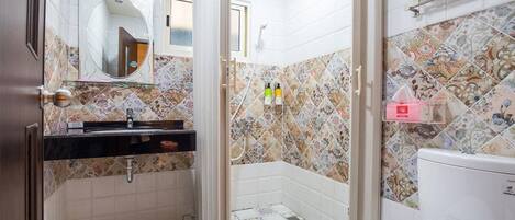 Un baño con ducha, inodoro y lavabo, con azulejos estampados y un espejo.
