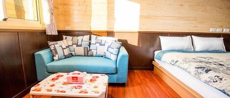 Una habitación con un sofá azul, una cama con ropa de cama estampada, piso de madera y una mesita con mantel floral.