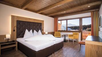 Habitación de hotel con una cama grande, mesitas de noche, un escritorio y una silla. Hay una ventana con vistas a las montañas.