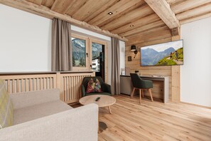 Una habitación acogedora con techo de madera, un sofá, una silla, una mesita, un televisor y una ventana con vistas a la montaña.