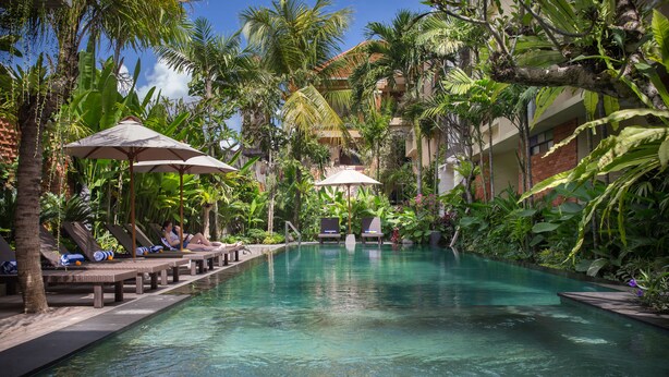 A pool area with lounge chairs and umbrellas, surrounded by lush tropical plants. - Grand Sehati & Spa Ubud (Ubud)