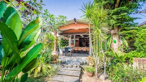 A covered outdoor seating area with tables and chairs, surrounded by lush greenery and plants. - Phuket Monaburi Boutique Hotel (Rawai)