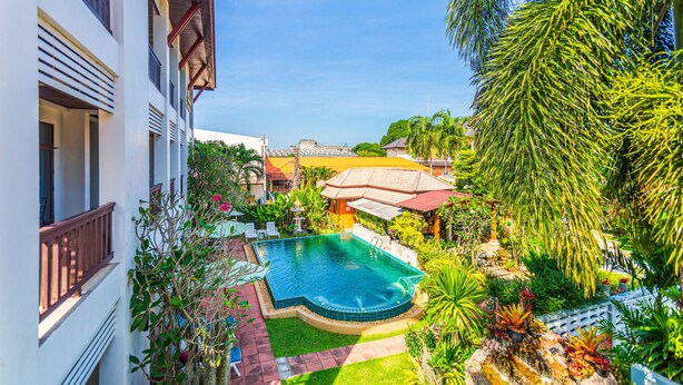A swimming pool surrounded by lush greenery and a building with balconies.