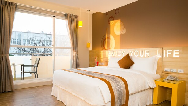 A hotel room with a large bed, a bedside table with a phone, and a view of the outside through a large window. - Bai Sha Tan Cottage (Hengchun)