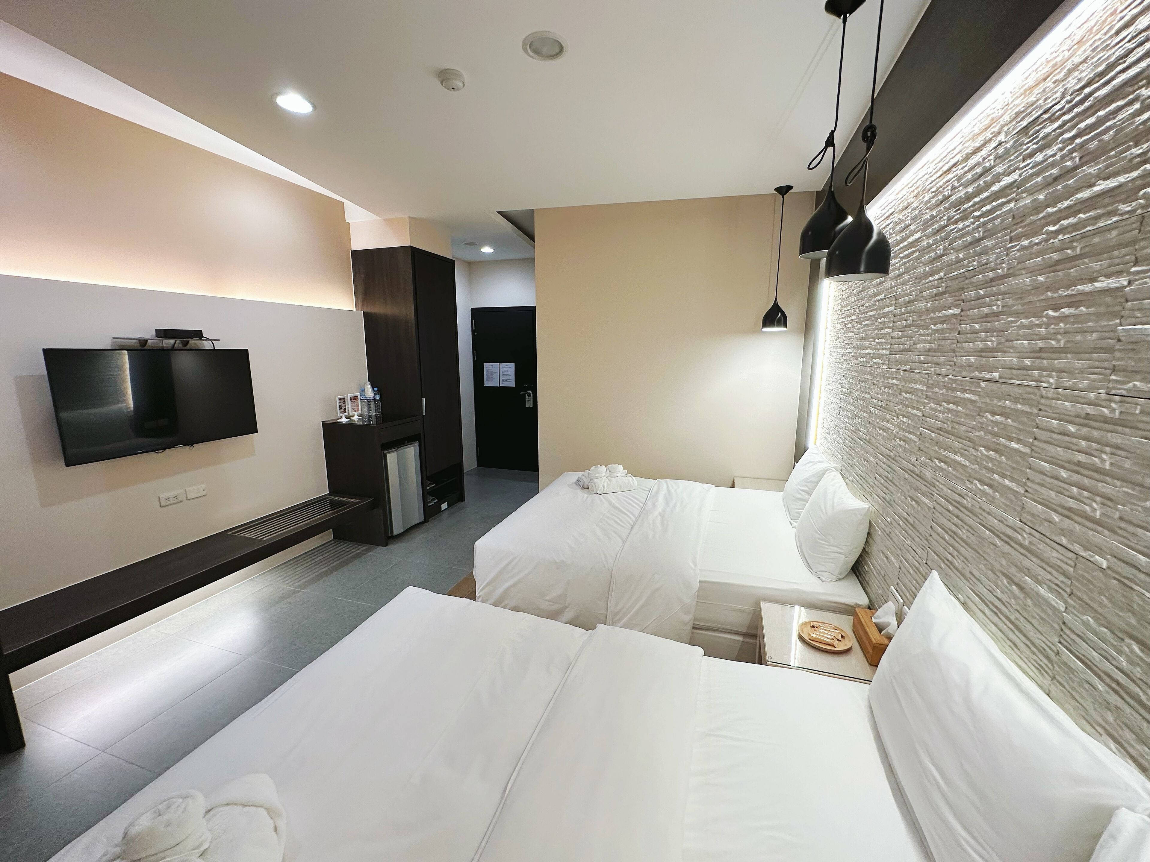 Een moderne hotelkamer met een flatscreen televisie, twee bedden, een klein bureau en een wandradiator.
