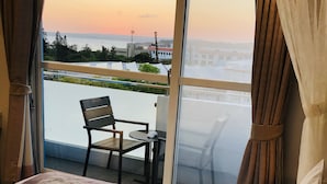 A hotel room with a bed, two pillows, a pair of towels, and a view of a balcony with a chair and table. - Bai Sha Tan Cottage (Hengchun)