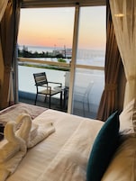 A hotel room with a bed, two pillows, a pair of towels, and a view of a balcony with a chair and table.