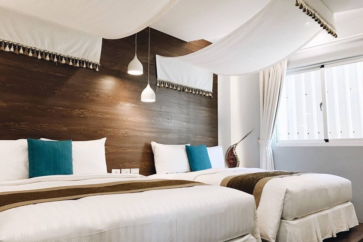 A double bed with white and teal pillows, a wooden headboard, and a hanging light fixture.