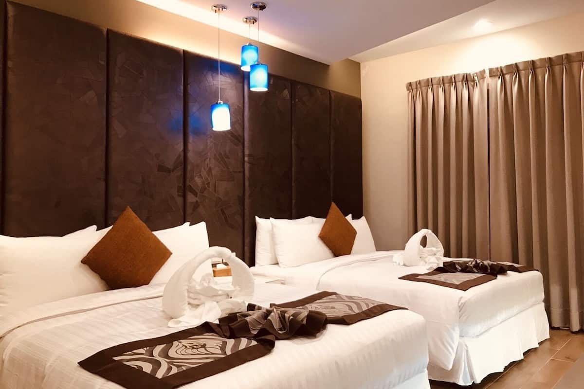 A hotel room with two beds, dark headboard panels, a large window with curtains, and a ceiling light fixture.