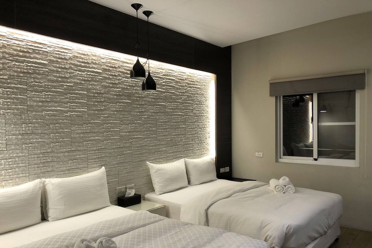 A modern hotel room with two beds, a textured wall, and a window with a view.