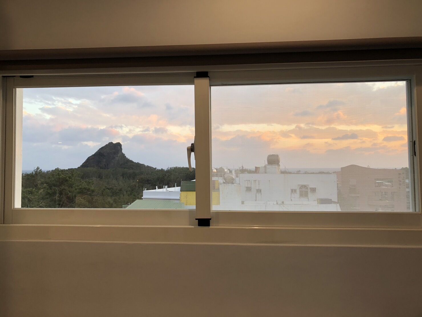 A window with a view of a mountain, buildings, and a cloudy sky.