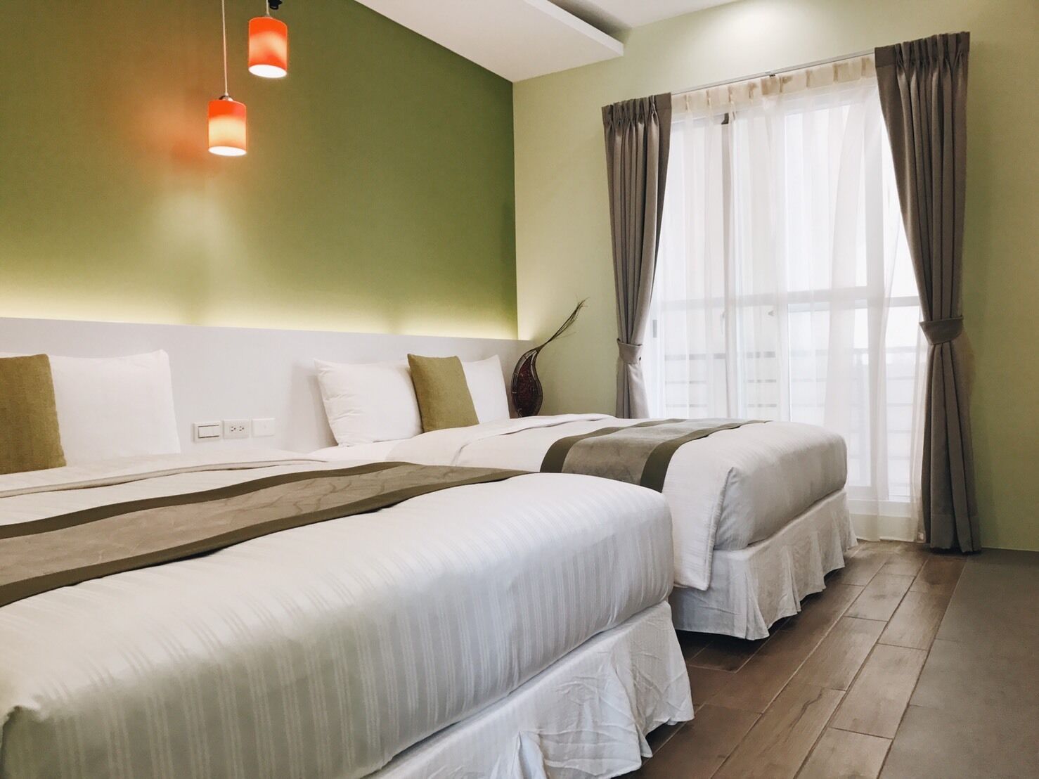 A hotel room with two beds, a green wall, and a window with curtains.