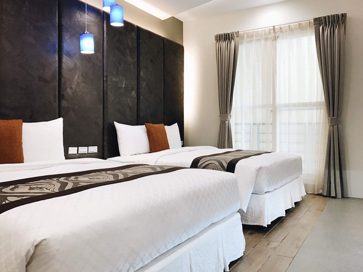A hotel room with two beds, a dark headboard, and a large window with curtains.