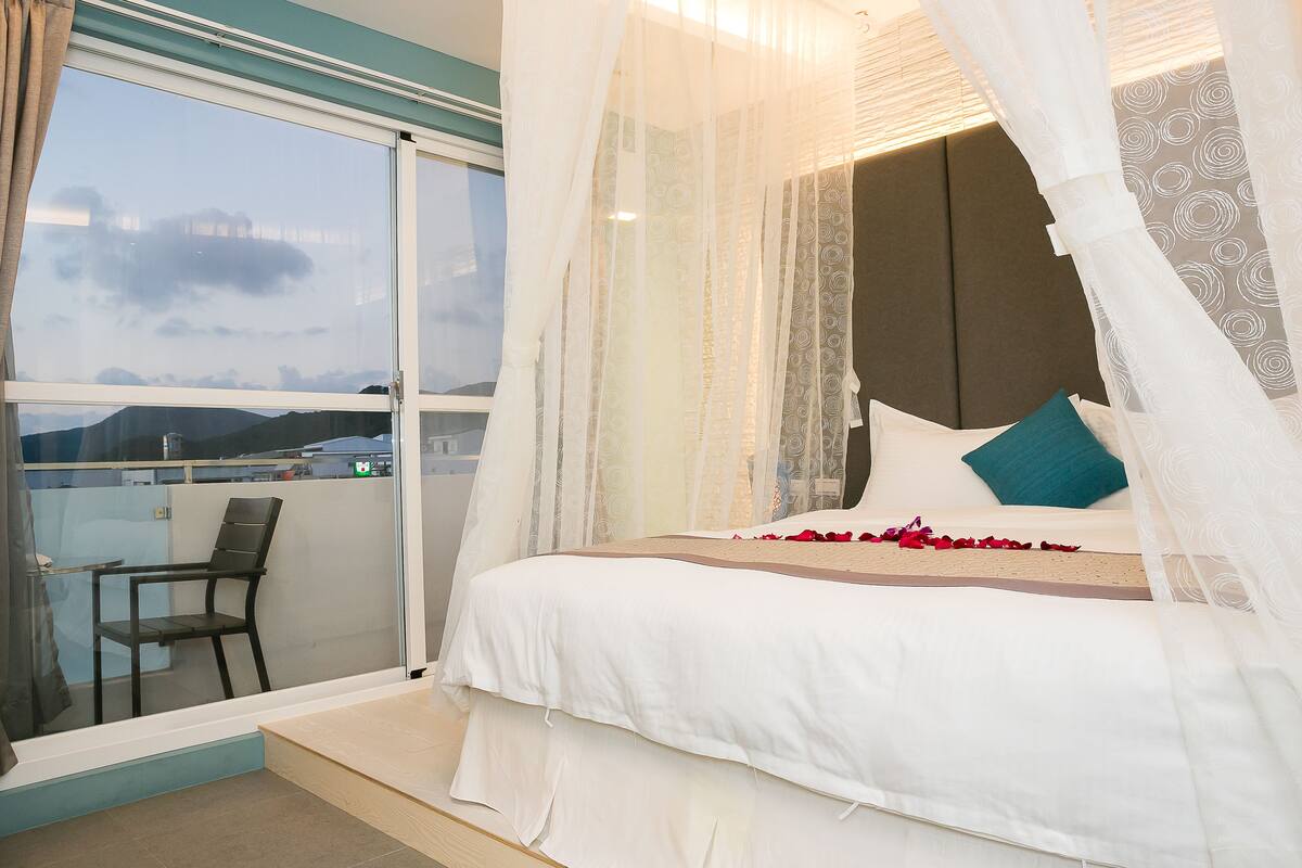 A bedroom with a bed, a chair, and a balcony with a view.