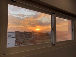 A view through a window of a sunset over a cityscape with buildings and a track.