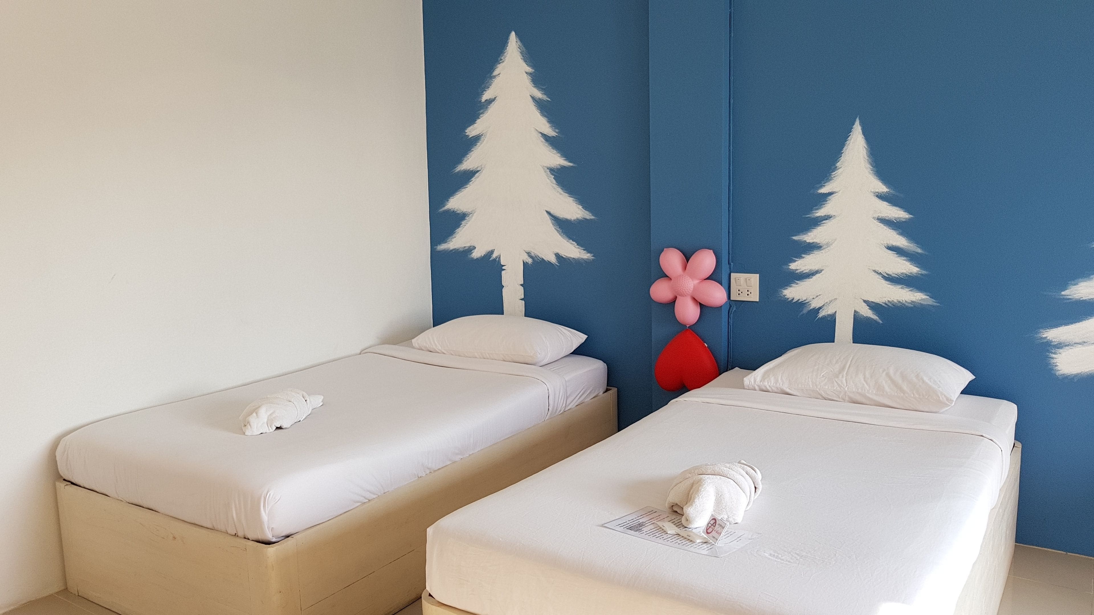 Two single beds with white linens, a blue accent wall, and a wall-mounted power outlet.