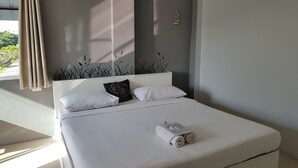 Una cama bien tendida con sábanas blancas, una toalla enrollada y dos almohadas, una lisa y otra con texto.