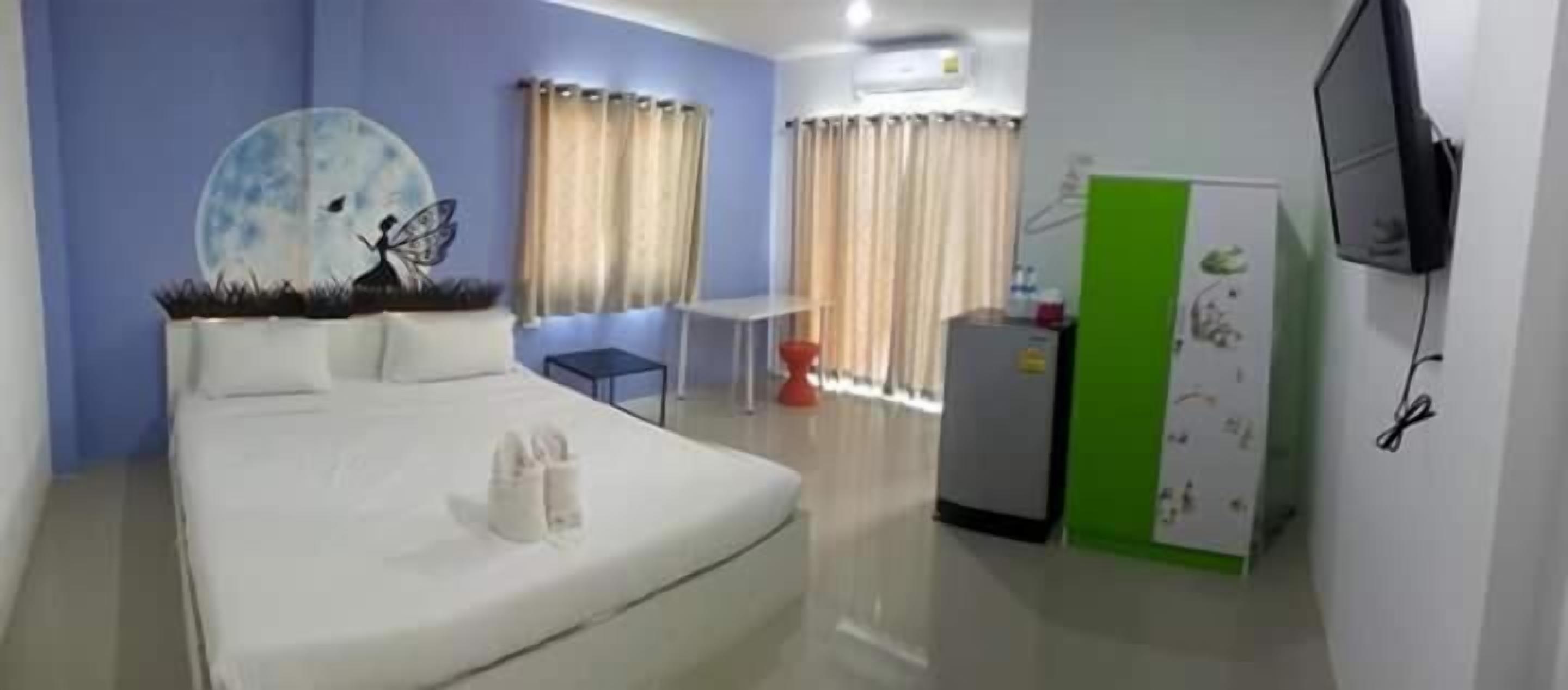A hotel room with a bed, a small table, a chair, a TV, and a green wall decoration.