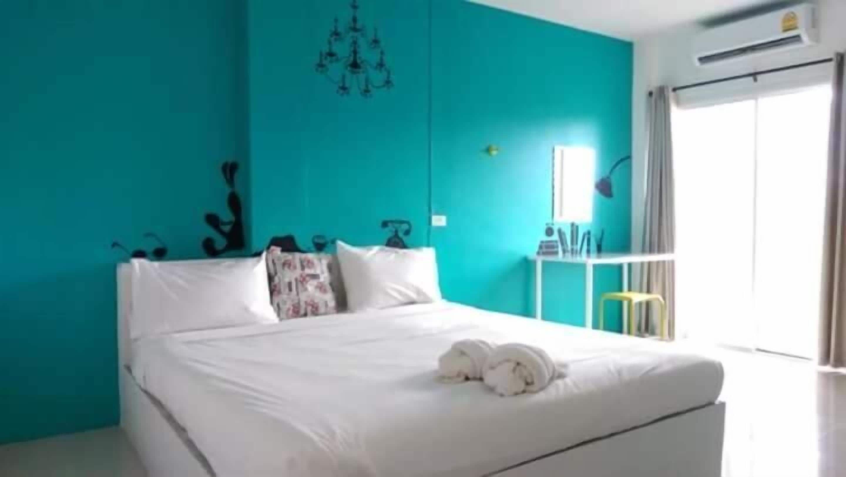 A bedroom with a bed, white bedding, a teal wall, a chandelier, and a window with curtains.