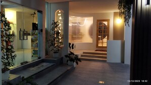 Entrada moderna de hotel con puerta de vidrio, escalones que conducen a la recepción y plantas decorativas.