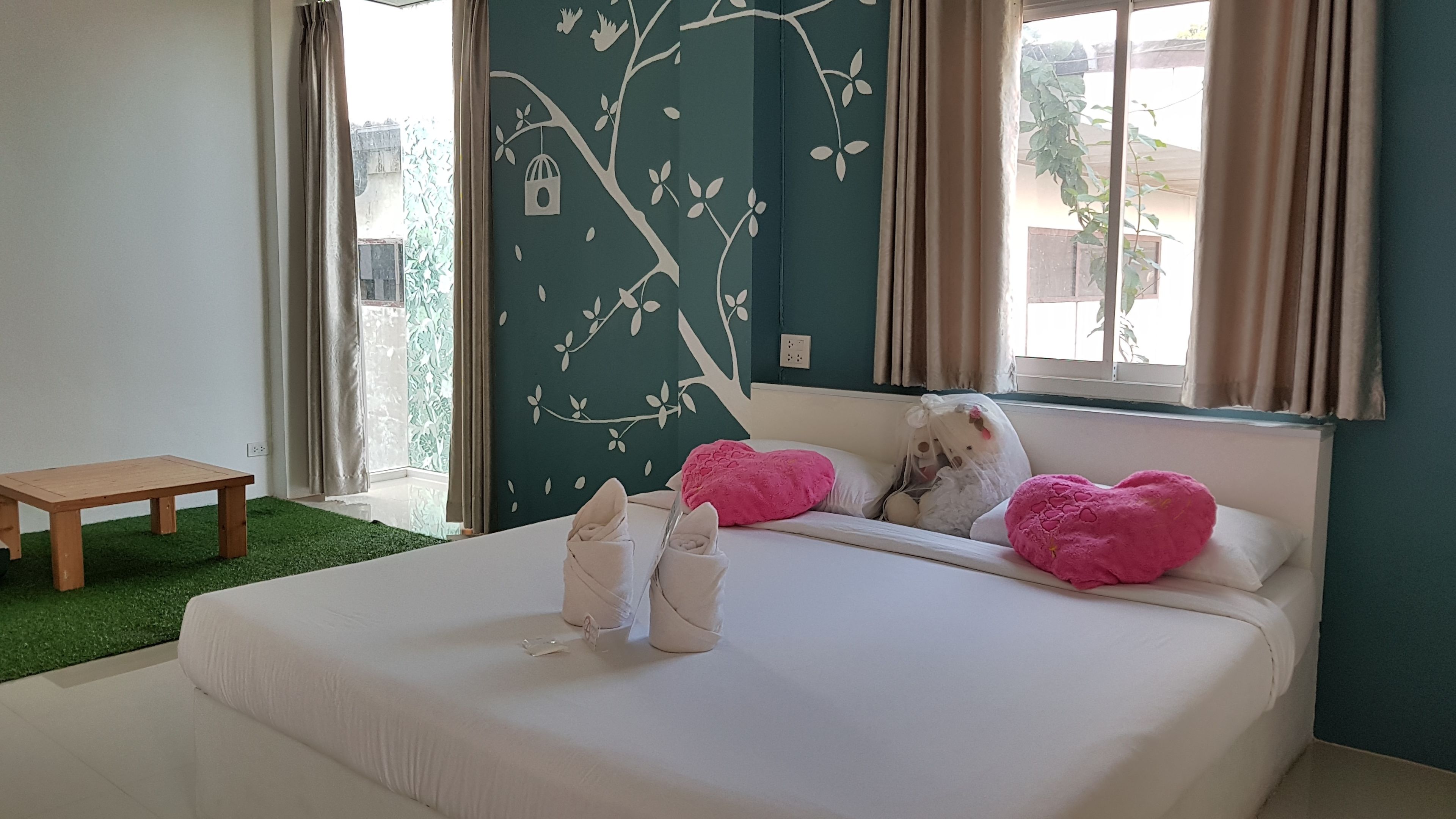 A bedroom with a bed, pillows, a bench, and a wall with a tree design.